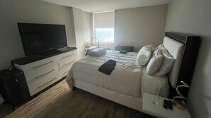 Ett sovrum med en säng, en tv, ett skrivbord och ett fönster.