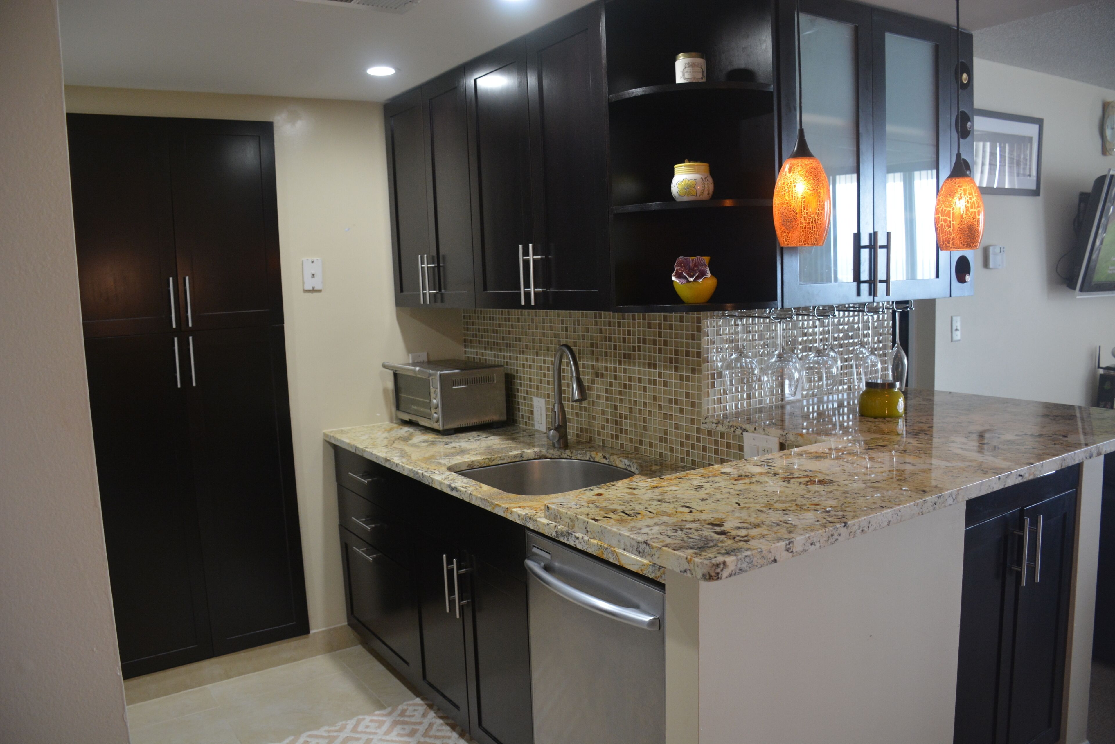A kitchen with dark cabinets, a granite countertop, a sink, a dishwasher, and two pendant lights.