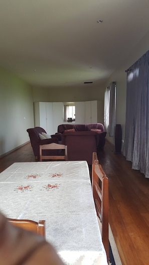 A spacious living area with a sofa set, a dining table with floral tablecloth, and a wardrobe.
