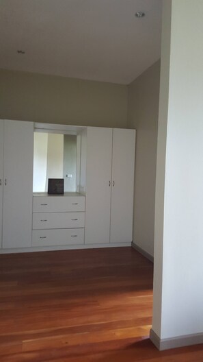A room with wooden flooring, white cabinets, and a mirror.