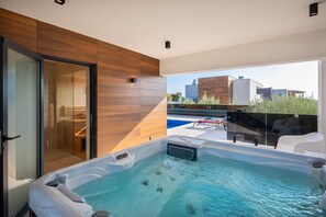 Ein moderner, überdachter Innenpool mit Glasfassade, Holzverkleidung und Blick auf Gebäude und Grünflächen.