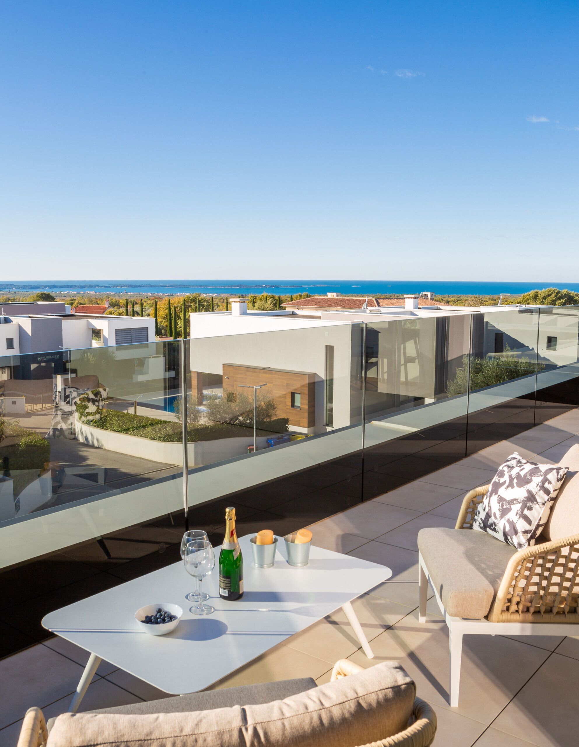 Une terrasse sur le toit avec une balustrade en verre, une table avec une bouteille et des verres, et un canapé.