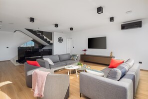 Ein modernes Wohnzimmer mit Treppe, grauen Sofas, einem Flachbildfernseher und Holzboden.