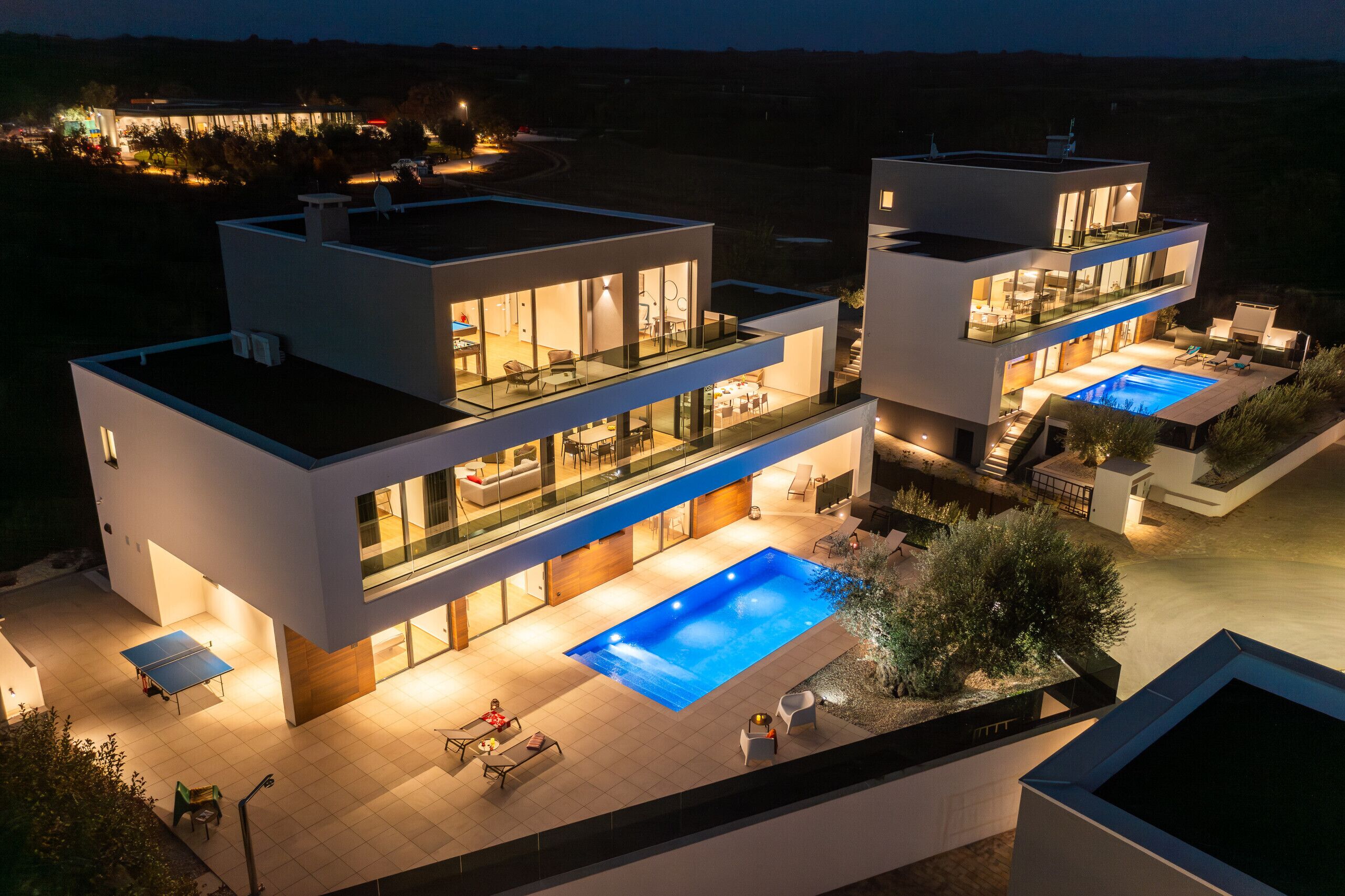 A modern two-story house with a swimming pool, outdoor seating, and a well-lit patio area.