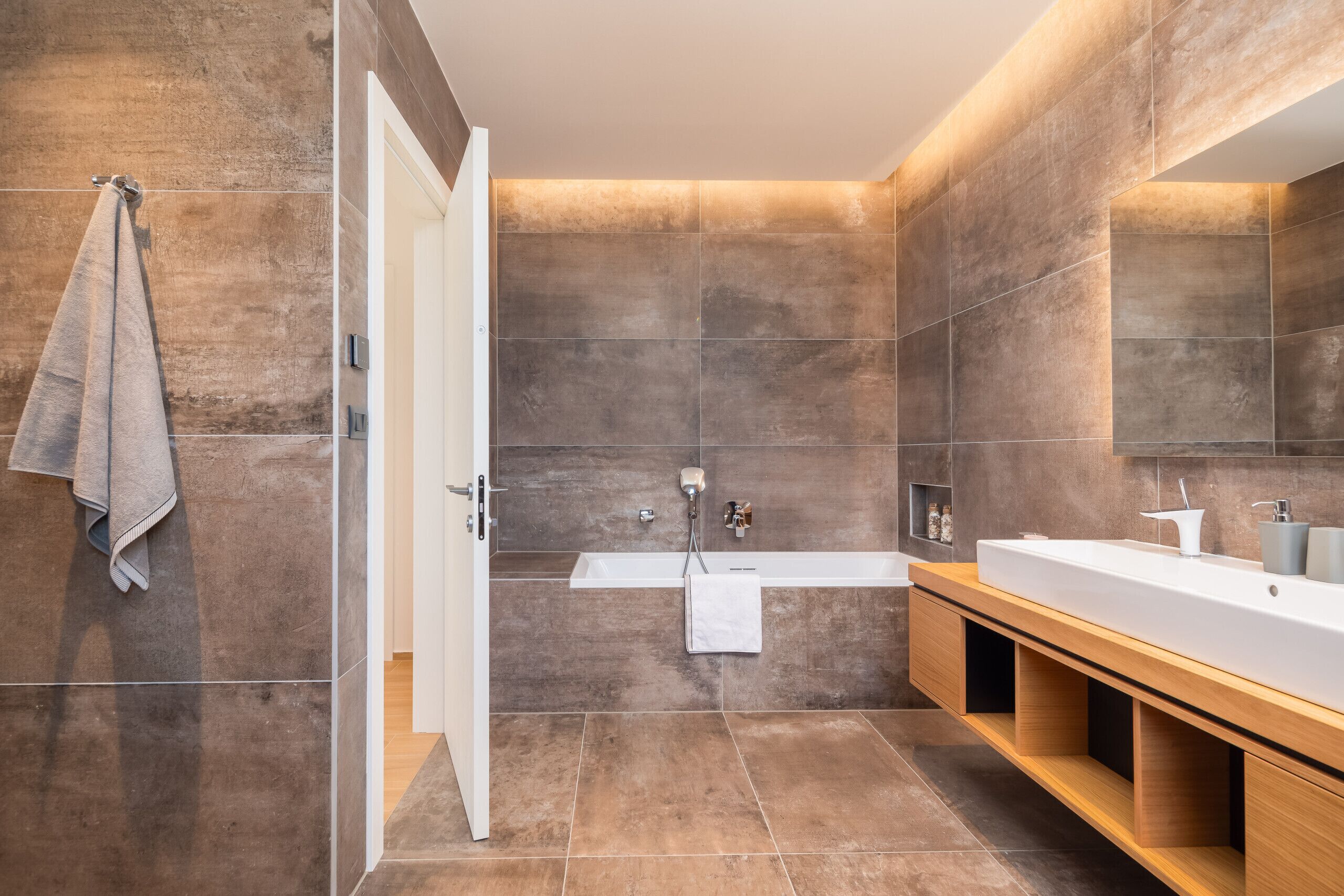 A modern bathroom with a large mirror, a bathtub, and a wooden vanity.