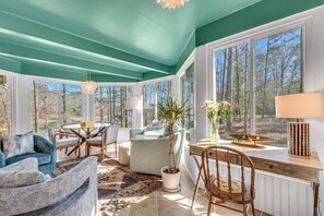 A sunlit room with a teal ceiling, large windows, a dining area, and a seating area with a rug.