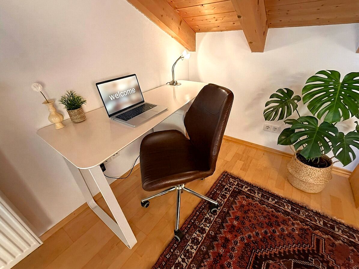 A workspace with a laptop, a brown chair, a white desk, a wooden ceiling, and a potted plant.