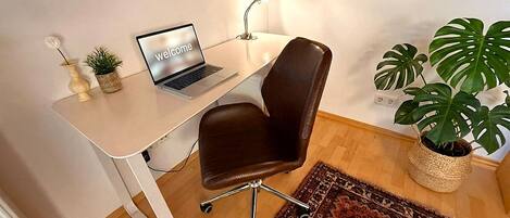 A workspace with a laptop, a brown chair, a white desk, a wooden ceiling, and a potted plant.