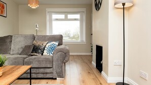 A living room with a grey sofa, a wooden coffee table, a floor lamp, a fireplace, and a window with a view.