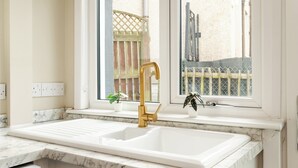 A kitchen with a white sink, gold faucet, and a window with a view of a fence and buildings.