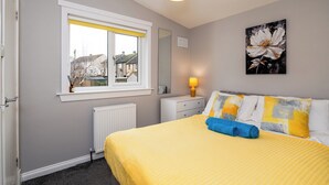 A bedroom with a bed, a window, a radiator, a bedside table with a lamp, and a painting on the wall.
