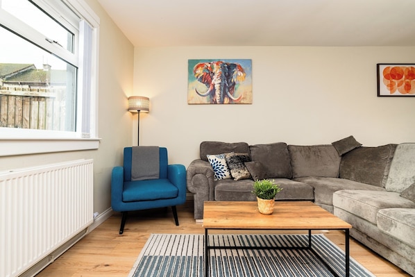 Un salon avec un fauteuil bleu, un canapé gris, une table basse en bois et un tableau représentant un éléphant accroché au mur.