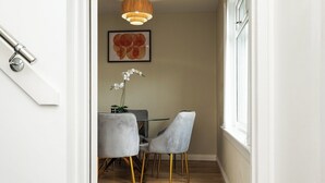 A narrow hallway with a dining area featuring two chairs and a table, a hanging light fixture, and a framed artwork on the wall.