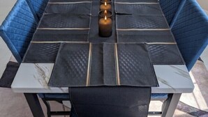 Een eettafel met blauwe fauteuils, een tafelkleed met marmerprint en een vaas met kaarsen.