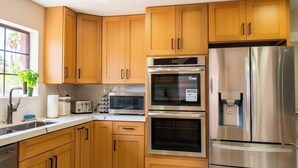 Een moderne keuken met houten kastjes, roestvrijstalen apparatuur en een raam met een plant.