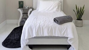 Een slaapkamer met een bed, nachtkastje, lamp en een potplant.