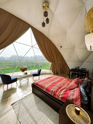Una amplia habitación con carpa, una cama grande, dos sillas, una mesita con flores y vistas al exterior.