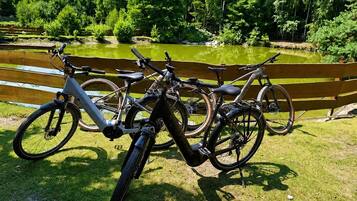 Des vélos sont garés près d’un banc en bois, au bord d’un étang, avec des arbres en arrière-plan.