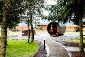 Una cabaña rústica con una estructura en forma de barril, rodeada de árboles y una valla de madera.