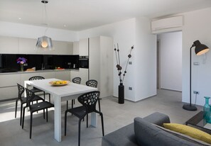 Eine moderne Küche mit weißen Schränken, einem Esstisch mit schwarzen Stühlen und einem grauen Sofa im Wohnbereich.