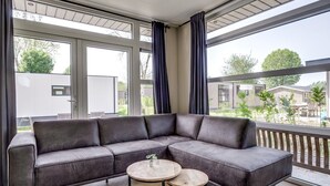 A modern living room with a sectional sofa, two round wooden tables, and large windows with curtains.