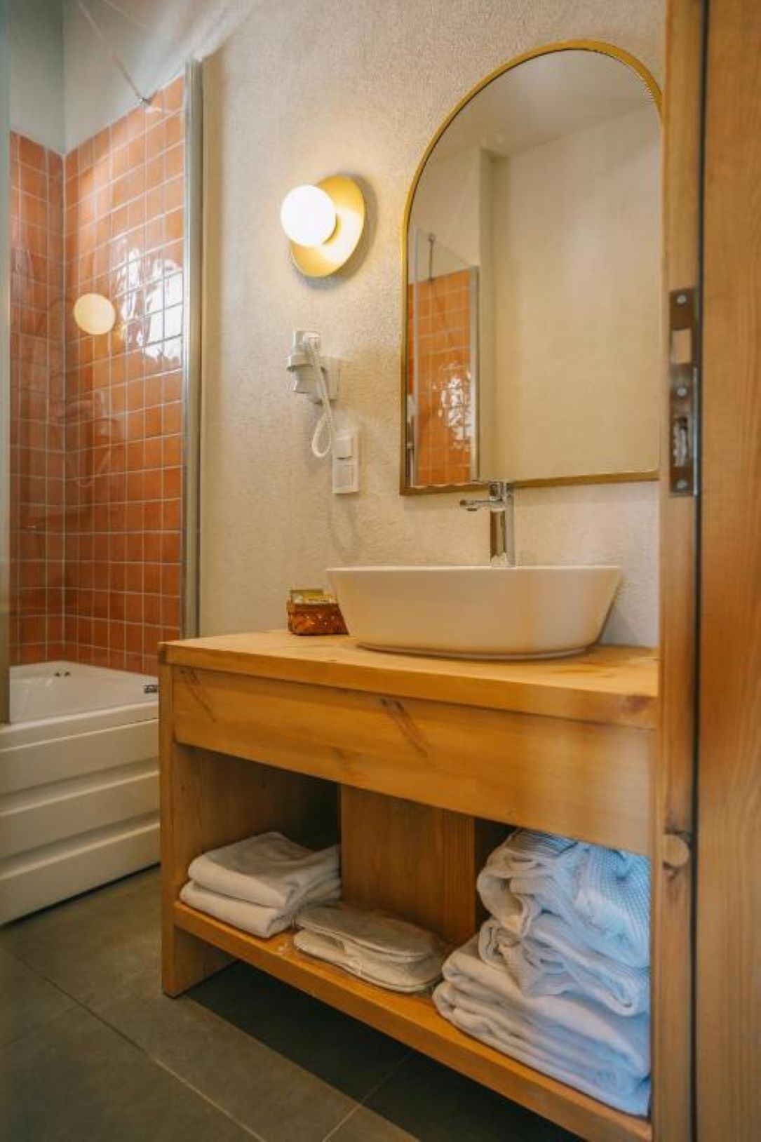 Un baño con lavamanos blanco, tocador de madera, espejo, toallero y bañera.