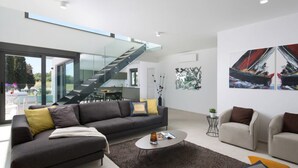Un salon moderne avec un canapé, une table basse et des fauteuils, un escalier et des œuvres d’art abstraites accrochées au mur.