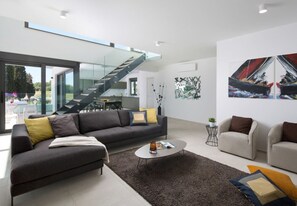 A modern living room with a sofa, coffee table, and armchairs, a staircase, and abstract wall art. - Vivi Rent Fažana - Villa Fasana Penthouse 5 (Fažana)