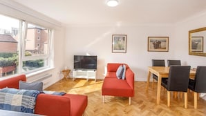 A modern living room with a red sofa, a TV, a dining table with chairs, and large windows offering a view of buildings outside. - Monkgate Cloisters - Free Parking (York)