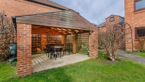 A brick house with a covered patio area, a table with chairs, and a small tree. - Monkgate Cloisters - Free Parking (York)
