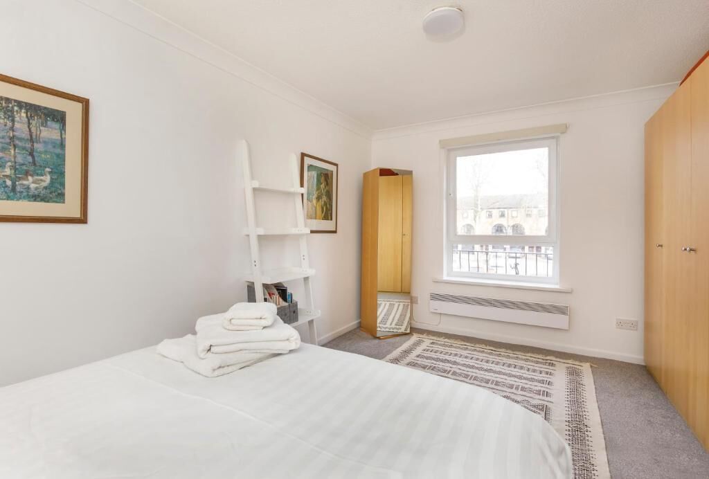 Une chambre à coucher avec un lit, une fenêtre, un radiateur, une armoire et un tableau au mur.