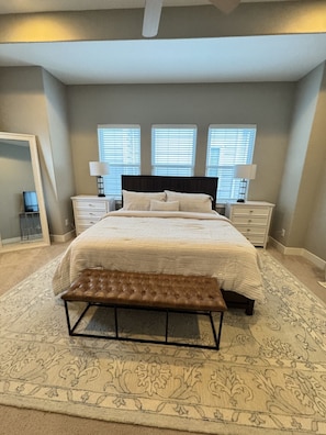 A bedroom with a large bed, two bedside tables, a bench, and three windows with blinds. - Spacious 3-Story Heights Townhome • 3 King Beds (Houston)