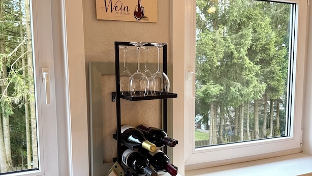 A room with a wine rack, a small house decoration, and a wooden tray with a Christmas tree design. - Cozy vacation apartment in Hahnenklee/Harz right on the edge of the forest with a large garden (Goslar)