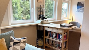 A cozy room with a window seat, a bookshelf, and a small table. - Cozy vacation apartment in Hahnenklee/Harz right on the edge of the forest with a large garden (Goslar)