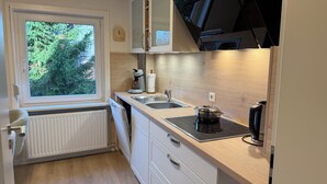 A compact kitchen with a window, a built-in stove, a sink, and a microwave. - Cozy vacation apartment in Hahnenklee/Harz right on the edge of the forest with a large garden (Goslar)