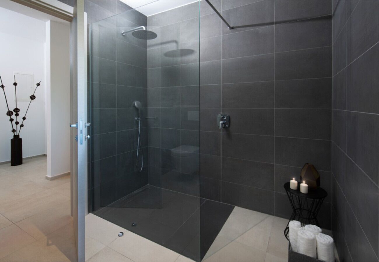 A modern bathroom with a glass-enclosed shower, dark tiles, and a small table with candles.