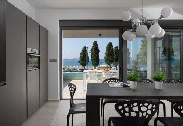 A modern kitchen with a view of the sea, a dining area with a table and chairs, and a balcony with potted plants. - Vivi Rent Fažana - Villa Fasana Penthouse 5 (Fažana)