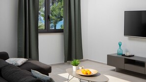 Ett modernt vardagsrum med en soffa, ett soffbord med en växt och frukt, en tv och ett grått skåp.