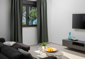 A modern living room with a sofa, a coffee table with a plant and fruit, a TV, and a grey cabinet. - Vivi Rent Fažana - Villa Fasana Penthouse 5 (Fažana)