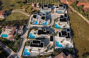 Eine Vogelperspektive auf einen modernen Wohnkomplex mit mehreren Häusern, Schwimmbecken und angelegten Gärten.