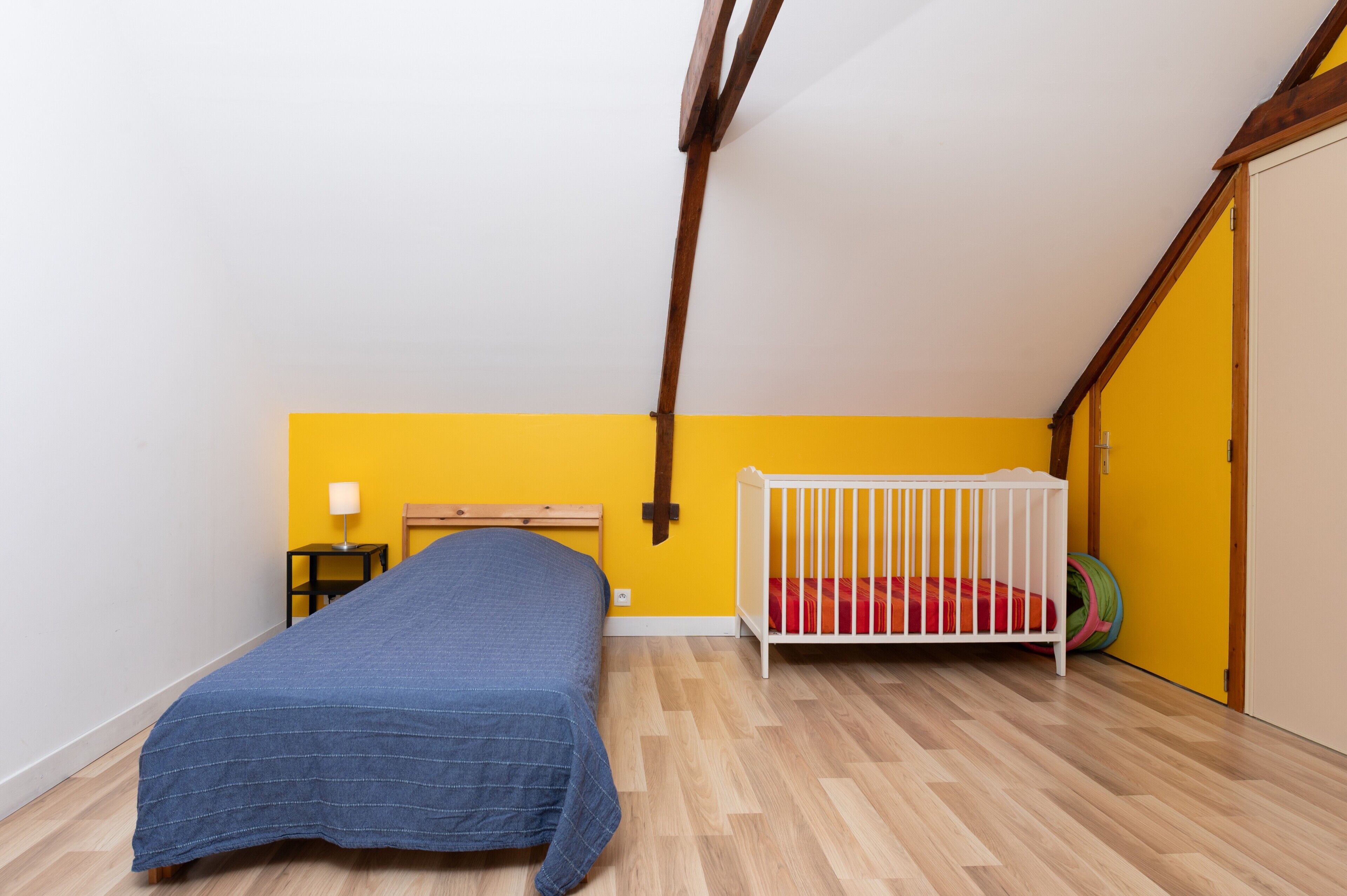 Een kamer met een bed, een ledikant, een klein tafeltje en een lamp.
