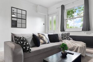 Un salon moderne avec un canapé gris, des coussins à motifs, une petite plante en pot et une table basse noire.