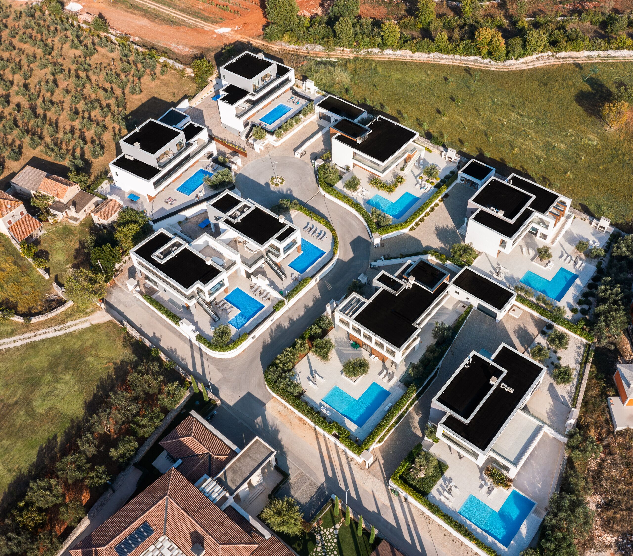 Een modern wooncomplex met meerdere huizen, elk met een dakterraszwembad en een ruim buitengebied.