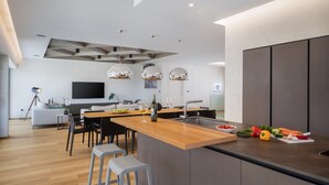 Una cucina moderna con isola centrale, zona pranzo e angolo salotto con divano e TV.