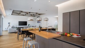 Eine moderne Küche mit Kochinsel, Essbereich und Wohnbereich mit Sofa und Fernseher.