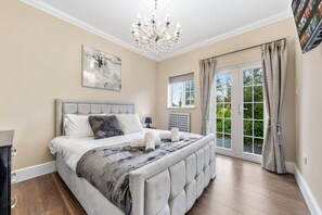 Une chambre à coucher avec un grand lit, un lustre, une fenêtre avec des rideaux et une vue sur la verdure à l’extérieur.