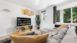 Ein modernes Wohnzimmer mit einer Couch, einem Fernseher, einer Pflanze und einem Fenster mit Blick auf Bäume.