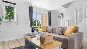 Ein modernes Wohnzimmer mit einem grauen Sofa, einem Holztisch und Blick auf ein Backsteingebäude durch große Fenster.