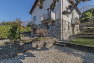 Un edificio de dos pisos con paredes de piedra, balcones y un camino de grava.