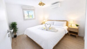 Ein Hotelzimmer mit Bett, zwei Nachttischlampen, einem Fenster, einer Klimaanlage und einem Blumentopf.